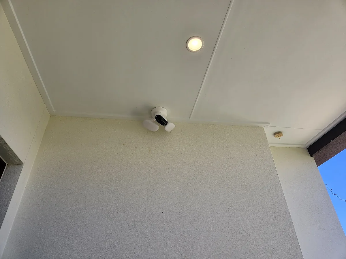 Porch ceiling with a recessed downlight and a floodlight camera mounted at the wall line