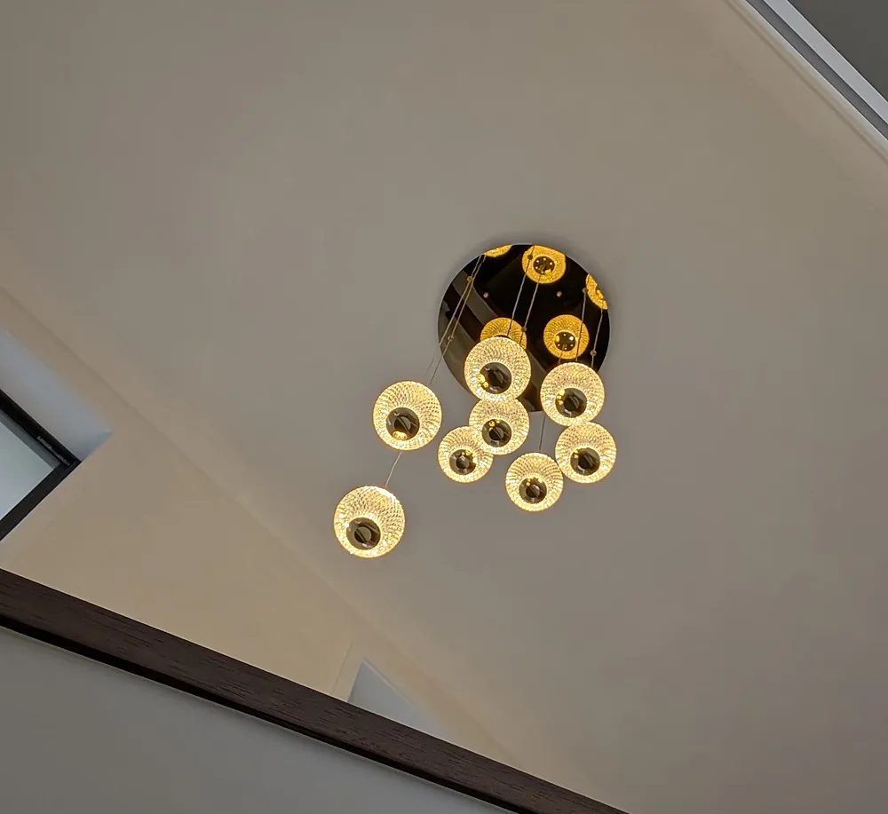 Cluster of glowing glass pendant globes hanging from a gold ceiling canopy in a stairwell void