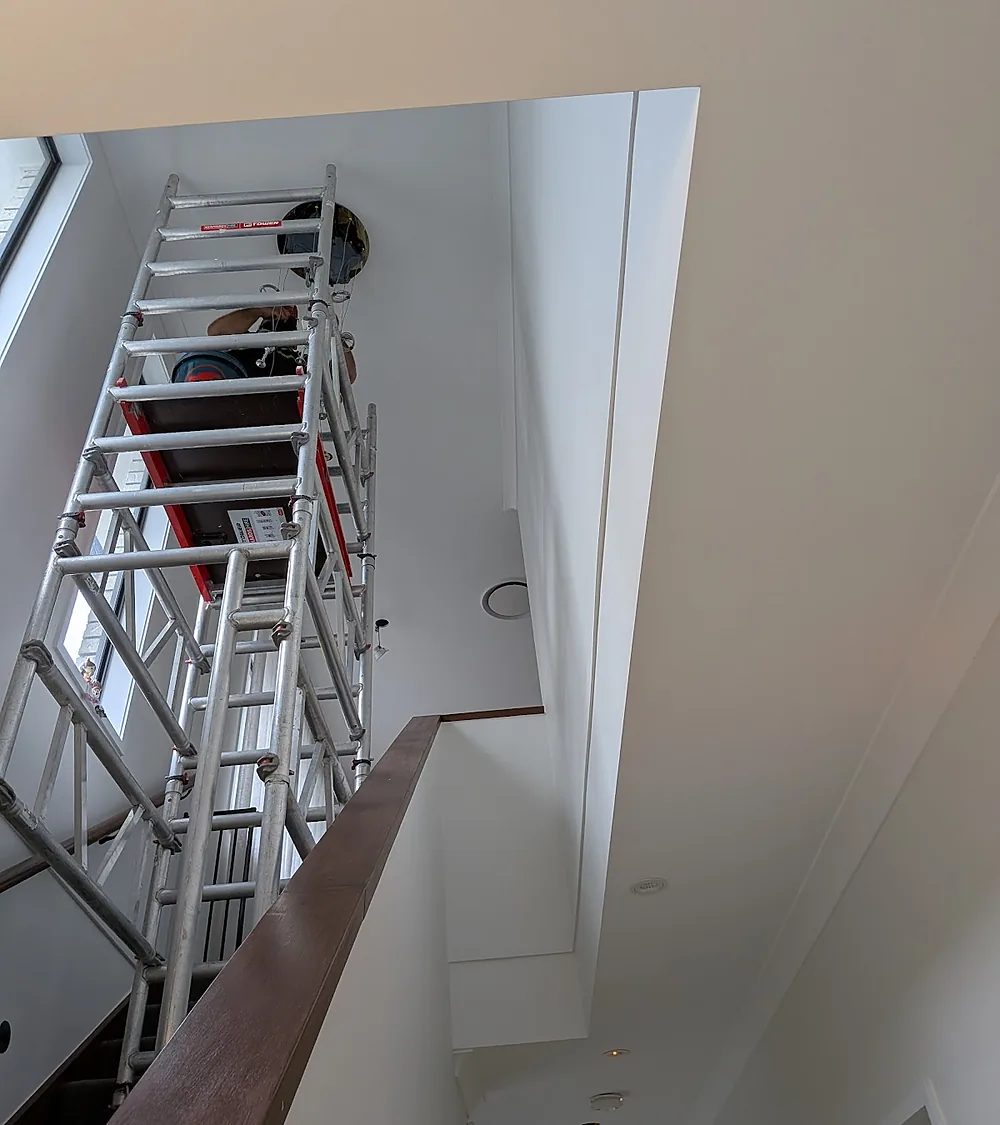 Electrician working from a mobile scaffold tower at a high stairwell ceiling
